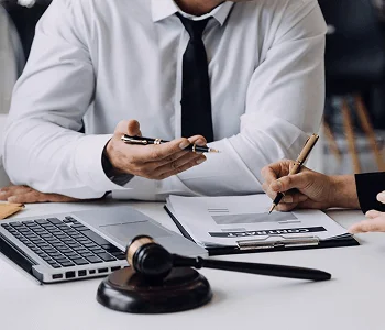 Two professionals discuss legal documents at a table, with a laptop and a gavel nearby, emphasizing a business or legal context.